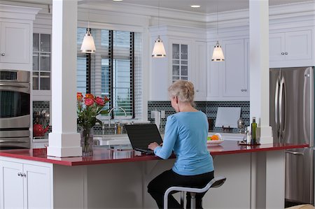 seniors back interior - Woman on laptop in kitchen of a Green Technology Home with energy efficiency appliances, stone countertops, and recycled wood Stock Photo - Premium Royalty-Free, Code: 6105-05397280
