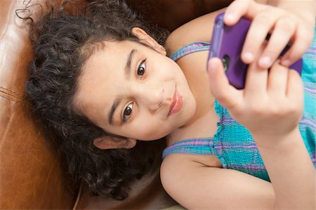 sending - Hispanic girl lying on a couch and looking at a text message on a mobile phone Foto de stock - Sin royalties Premium, Código: 6105-05397216