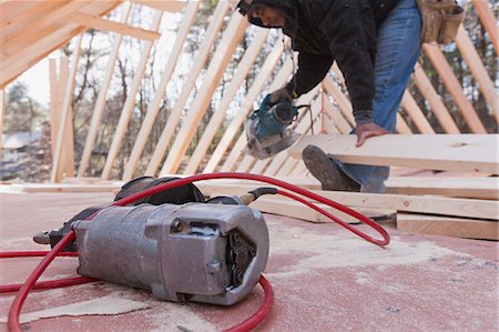 simsearch:6105-06043034,k - Carpenter cutting rafter using a circular saw with a nail gun on foreground Stock Photo - Premium Royalty-Free, Code: 6105-06042992