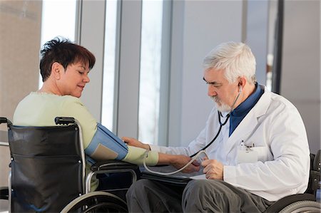 Doctor with muscular dystrophy in wheelchair checking the blood pressure of a patient Stock Photo - Premium Royalty-Free, Code: 6105-06043118