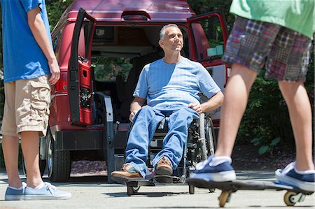 parent and child sports - Man with spinal cord injury in wheelchair watching his son on skateboard Stock Photo - Premium Royalty-Free, Code: 6105-06702996