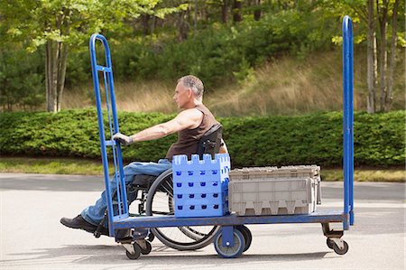 dolly - Loading dock worker with spinal cord injury in a wheelchair moving a hand truck Stock Photo - Premium Royalty-Free, Code: 6105-06703062