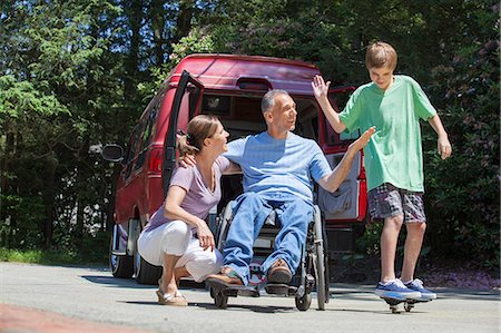 parent and child sports - Man with spinal cord injury in wheelchair giving high-five to son on skateboard Stock Photo - Premium Royalty-Free, Code: 6105-06703001