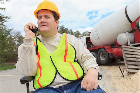 Construction supervisor with Spinal Cord Injury on walkie talkie with concrete mixer truck Stock Photo - Premium Royalty-Free, Code: 6105-07744502