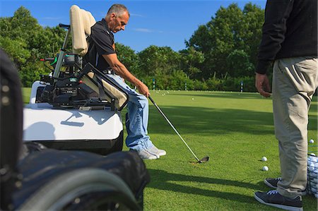 Man with a spinal cord injury in an adaptive cart at golf putting green with an instructor Stock Photo - Premium Royalty-Free, Code: 6105-08211343