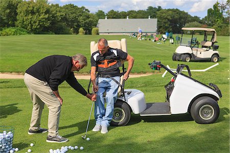 Man with a spinal cord injury in an adaptive cart at golf putting green with an instructor Stock Photo - Premium Royalty-Free, Code: 6105-08211342