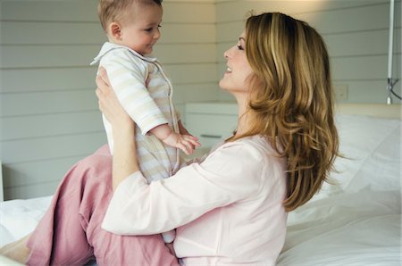 emotional images of mother holding baby - Woman and baby sitting on the bed, in profile Stock Photo - Premium Royalty-Free, Code: 6108-05855983