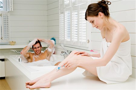 Couple in bathroom, man having a bath and woman wrapped in a towel shaving her legs Stock Photo - Premium Royalty-Free, Code: 6108-05856143