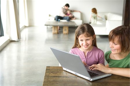 Woman and little girl using laptop computer, man and 2 children in the background Stock Photo - Premium Royalty-Free, Code: 6108-05856594
