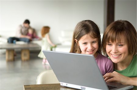 Smiling woman and little girl using laptop computer, man and 2 children in the background Stock Photo - Premium Royalty-Free, Code: 6108-05856620