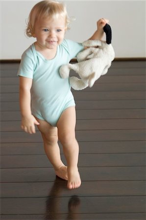 Little boy holding stuffed dog, walking on wooden floor, front view Stock Photo - Premium Royalty-Free, Code: 6108-05856622