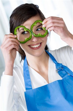 Young smiling woman holding 2 green pepper slices in front of her eyes Stock Photo - Premium Royalty-Free, Code: 6108-05857045