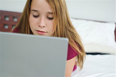 Teenage girl using laptop, lying on bed Stock Photo - Premium Royalty-Free, Code: 6108-05857750