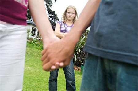 envy - Teenagers holding hands, teen girl with arms crossed in background, outdoors Stock Photo - Premium Royalty-Free, Code: 6108-05857782