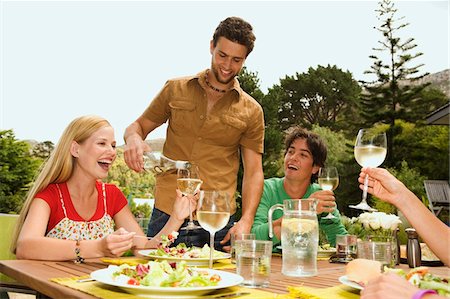 summer meal - 2 young smiling couples sitting at garden table, man pouring wine Stock Photo - Premium Royalty-Free, Code: 6108-05857859