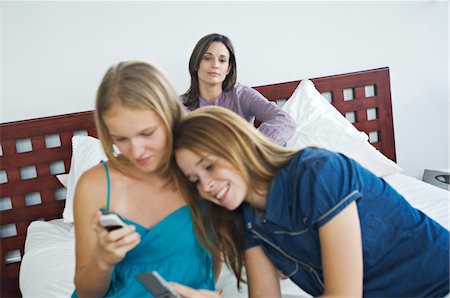 family indoors summer - 2 smiling teenage girls using mobile phones, woman in background Stock Photo - Premium Royalty-Free, Code: 6108-05857817