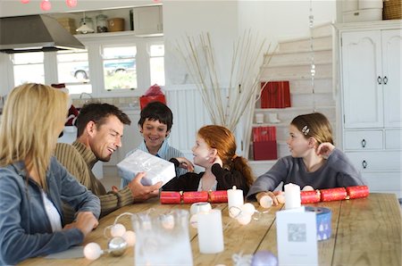 Couple ad three children sitting around table, exchanging Christmas presents, indoors Stock Photo - Premium Royalty-Free, Code: 6108-05858058