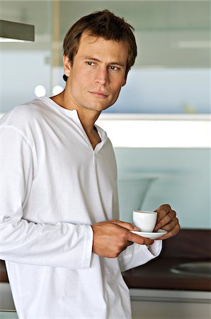 Young thinking man in kitchen, holding coffee cup Stock Photo - Premium Royalty-Free, Code: 6108-05859061