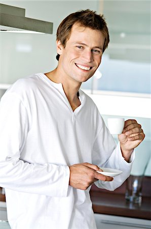 simsearch:6108-05856772,k - Young smiling man in kitchen, holding coffee cup Stock Photo - Premium Royalty-Free, Code: 6108-05859021