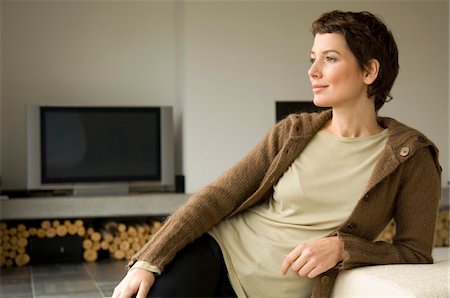 emotional woman looking away - Mid adult woman leaning against a couch Stock Photo - Premium Royalty-Free, Code: 6108-05859774