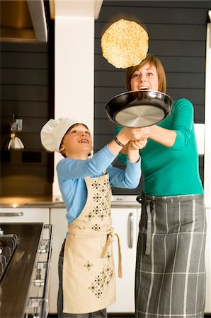 Young woman flipping a pancake with her son Stock Photo - Premium Royalty-Free, Code: 6108-05859849