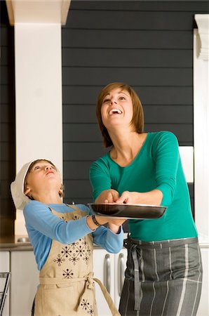 Young woman holding a frying pan with her son and smiling Stock Photo - Premium Royalty-Free, Code: 6108-05859894