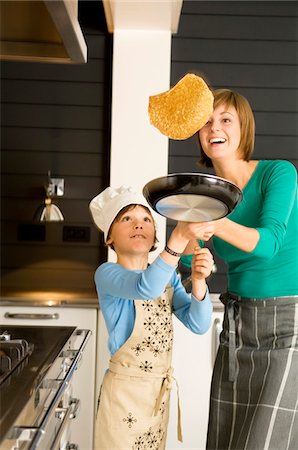 Young woman flipping a pancake with her son Stock Photo - Premium Royalty-Free, Code: 6108-05859899
