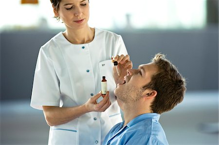 doctor giving medicine to adult patient - Female doctor giving medicine drops to a male patient Stock Photo - Premium Royalty-Free, Code: 6108-05860392