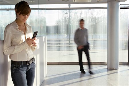 simsearch:6108-05860554,k - Businesswoman using a mobile phone with a businessman walking in the background Stock Photo - Premium Royalty-Free, Code: 6108-05860458