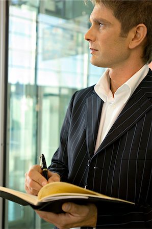 simsearch:6108-05860448,k - Close-up of a businessman writing in a diary and looking through a window Foto de stock - Sin royalties Premium, Código: 6108-05860502