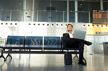 people airport - Businessman using a laptop and talking on a mobile phone Stock Photo - Premium Royalty-Free, Code: 6108-05860536