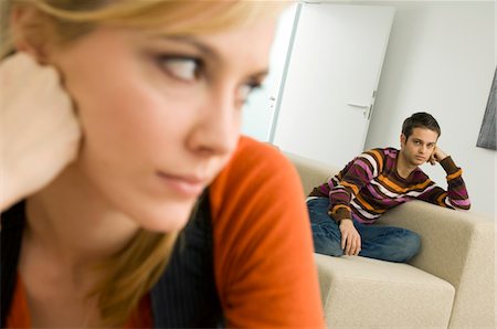 Close-up of a young woman thinking with a young man sitting on a couch in the background Stock Photo - Premium Royalty-Free, Code: 6108-05860712