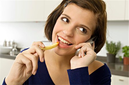 Close-up of a young woman eating French fries and talking on a mobile phone Stock Photo - Premium Royalty-Free, Code: 6108-05861066