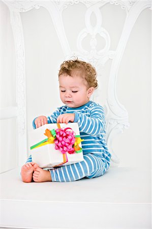 ribbon knot designs - Baby boy playing with a present in an armchair Stock Photo - Premium Royalty-Free, Code: 6108-05862684