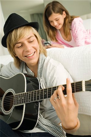 simsearch:6108-05863846,k - Adolescent jouant une guitare et sa soeur à l'aide d'un téléphone mobile derrière lui Photographie de stock - Premium Libres de Droits, Code: 6108-05862898