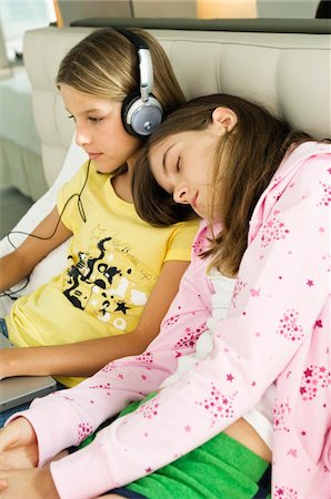 face to internet technology - Jeune fille travaillant sur un ordinateur portable et à l'écoute sur casque et sa sœur dort sur ses épaules Photographie de stock - Premium Libres de Droits, Code: 6108-05862982