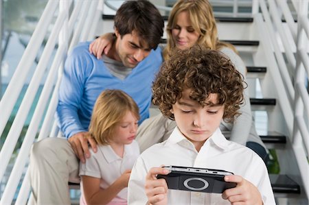 simsearch:6108-05860263,k - Parents sitting on steps with their children playing video games Stock Photo - Premium Royalty-Free, Code: 6108-05863415