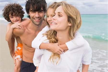 Couple giving piggyback ride to their children on the beach Stock Photo - Premium Royalty-Free, Code: 6108-05864044