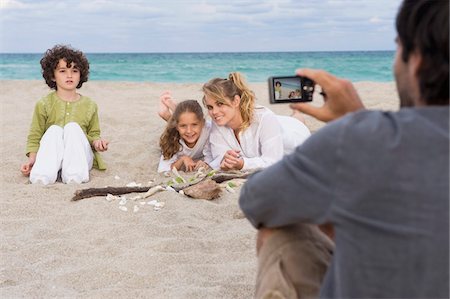 simsearch:6108-05863846,k - Homme qui prend une photo de sa famille avec un appareil photo numérique sur la plage Photographie de stock - Premium Libres de Droits, Code: 6108-05864054