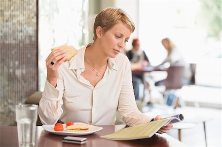 Businesswoman sitting in a restaurant and reading a magazine Stock Photo - Premium Royalty-Free, Code: 6108-05865778