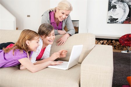 preteen girls looking older - Two girls using a laptop on a couch with their grandmother standing beside them Stock Photo - Premium Royalty-Free, Code: 6108-05867548