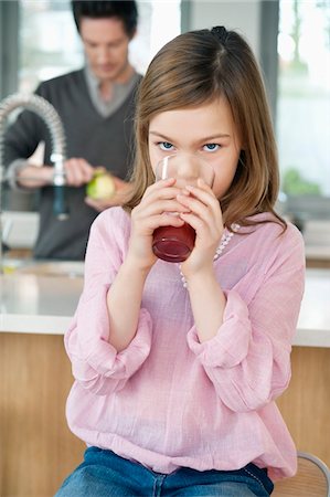Girl drinking juice with her father standing behind her Stock Photo - Premium Royalty-Free, Code: 6108-05867514