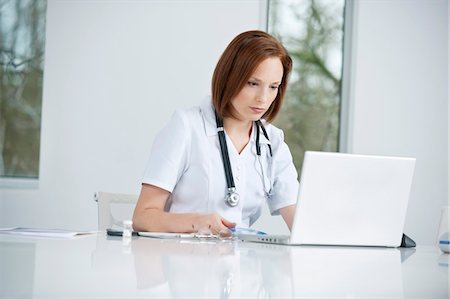 Female doctor sitting in an office inserting CD into a laptop Stock Photo - Premium Royalty-Free, Code: 6108-05867972