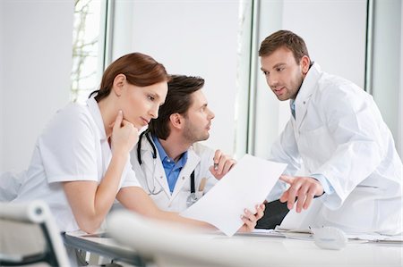 Three doctors examining a medical report Stock Photo - Premium Royalty-Free, Code: 6108-05868009
