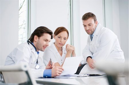 Three doctors examining a medical report Stock Photo - Premium Royalty-Free, Code: 6108-05868018