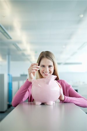 Businesswoman inserting a coin into a piggy bank Stock Photo - Premium Royalty-Free, Code: 6108-05868440