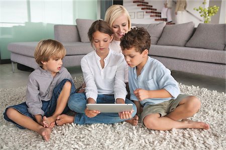 Girl using a digital tablet with her mother and brothers sitting beside her Stock Photo - Premium Royalty-Free, Code: 6108-05870058