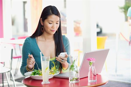 simsearch:6108-06166047,k - Woman reading text message while eating food in a restaurant Stock Photo - Premium Royalty-Free, Code: 6108-05870297