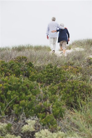 Rear view of a senior couple walking on the beach with their arms around each other Stock Photo - Premium Royalty-Free, Code: 6108-05871000