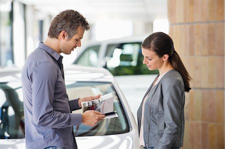 people car shopping - Side profile of a couple looking at catalog in car showroom Stock Photo - Premium Royalty-Free, Code: 6108-05871390